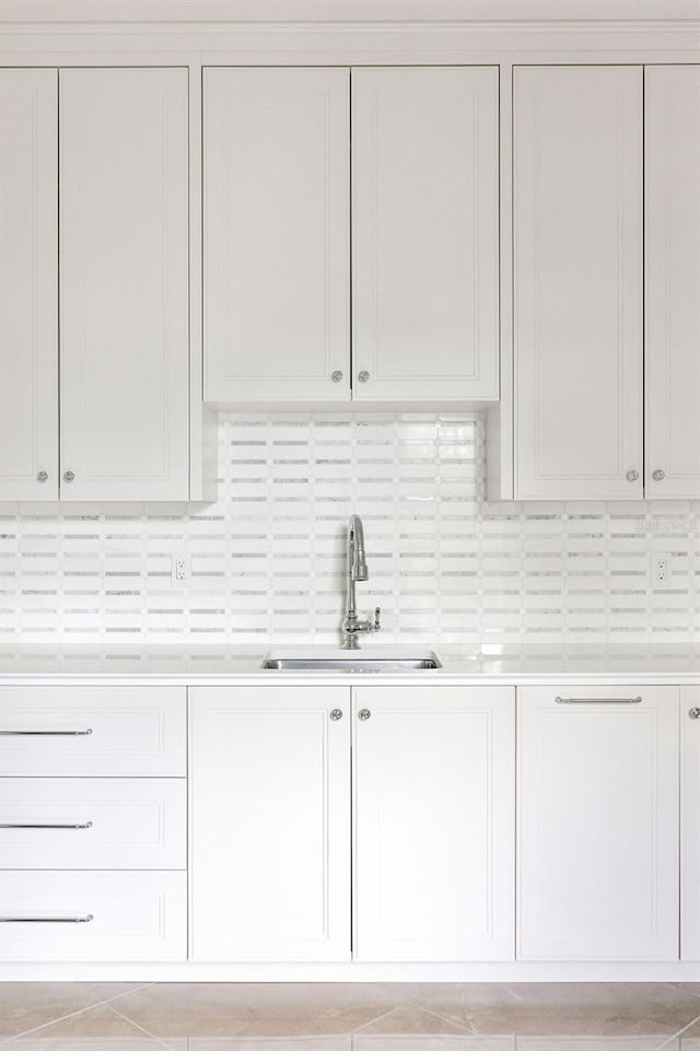 interior space with backsplash, sink, and white cabinetry