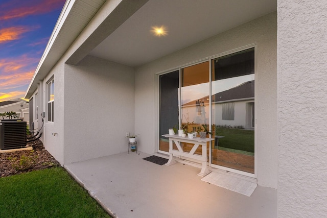 exterior entry at dusk with cooling unit and a patio