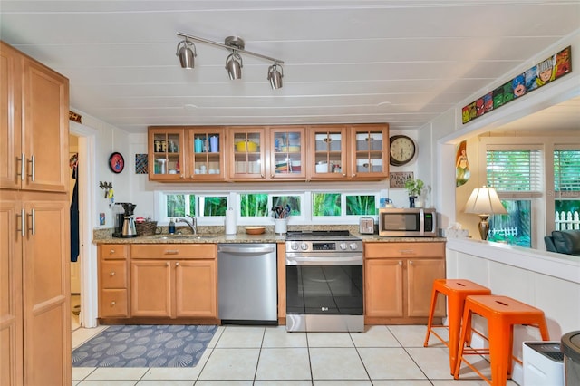 kitchen featuring light tile patterned flooring, appliances with stainless steel finishes, a healthy amount of sunlight, and light stone countertops