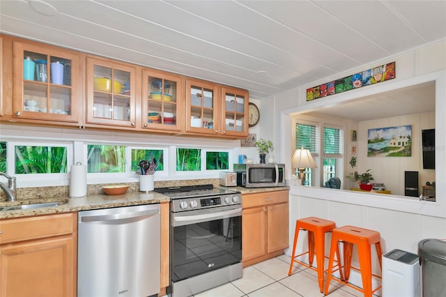 kitchen with light tile patterned floors, appliances with stainless steel finishes, sink, and light stone countertops