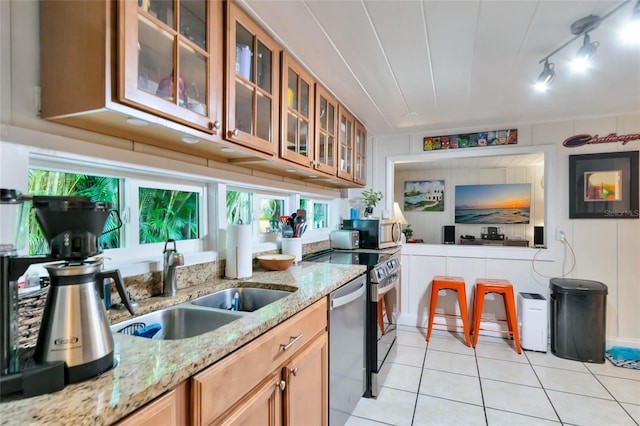 kitchen featuring appliances with stainless steel finishes, light tile patterned floors, light stone counters, and sink