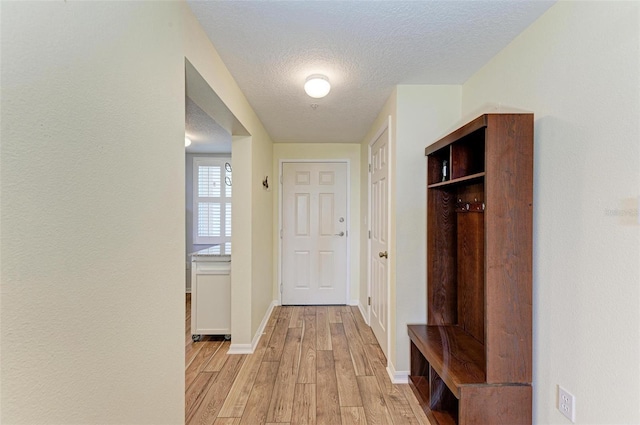 mudroom featuring light wood-style flooring, baseboards, and a textured ceiling