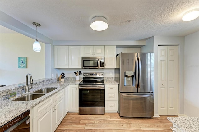 kitchen with light stone countertops, a sink, light wood-style floors, and appliances with stainless steel finishes