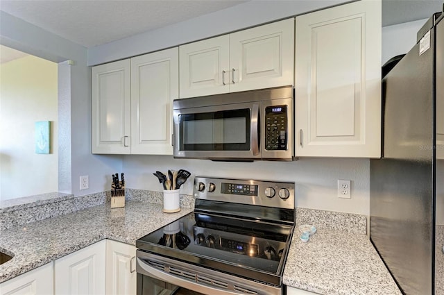 kitchen with appliances with stainless steel finishes, a textured ceiling, white cabinetry, and light stone countertops