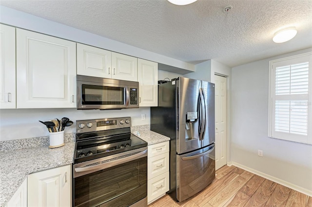 kitchen with appliances with stainless steel finishes, light hardwood / wood-style floors, light stone counters, white cabinets, and a textured ceiling