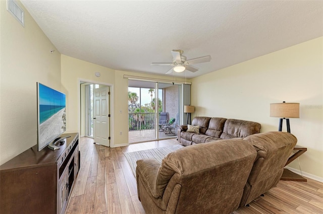 living area with light wood finished floors, a textured ceiling, baseboards, visible vents, and ceiling fan