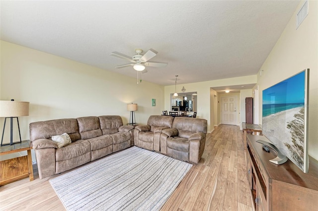 living room with light wood-type flooring, ceiling fan, and a textured ceiling