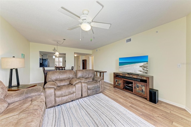 living area with a textured ceiling, visible vents, wood finished floors, and a ceiling fan