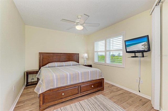 bedroom featuring baseboards, light wood-type flooring, ceiling fan, and a textured ceiling