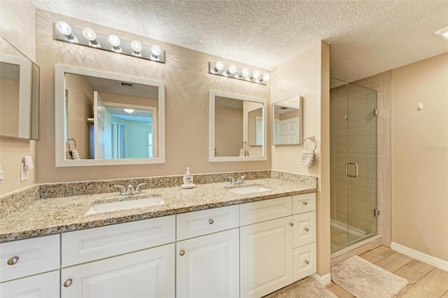 bathroom with a textured ceiling, wood-type flooring, a shower with door, and vanity