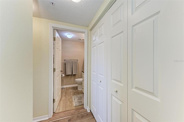 hall featuring a textured ceiling, baseboards, and wood tiled floor