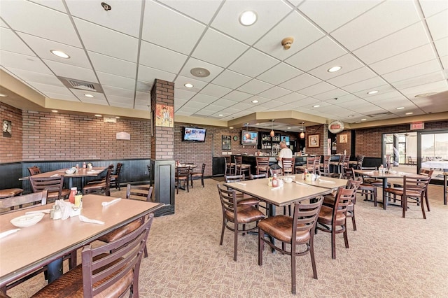 dining area featuring a drop ceiling, light colored carpet, and brick wall