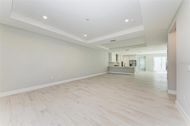 unfurnished living room featuring light wood-type flooring, a raised ceiling, and a textured ceiling