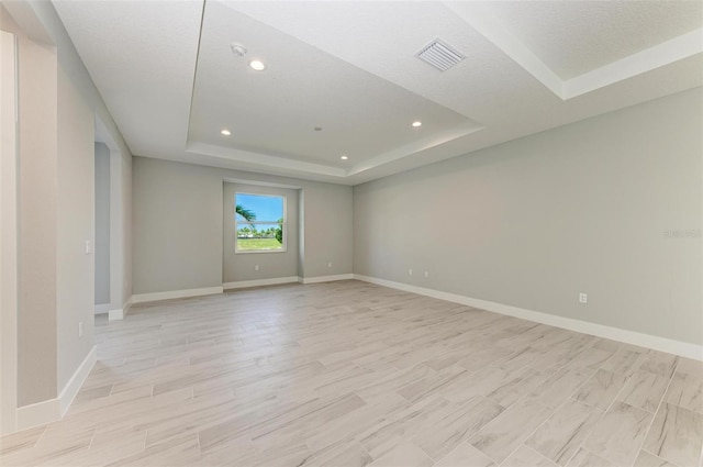 unfurnished room with a textured ceiling, a raised ceiling, and light hardwood / wood-style floors