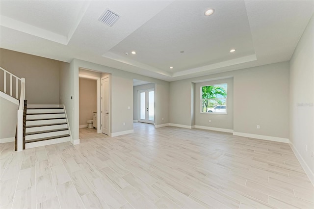 unfurnished living room featuring light hardwood / wood-style flooring, a tray ceiling, and a textured ceiling