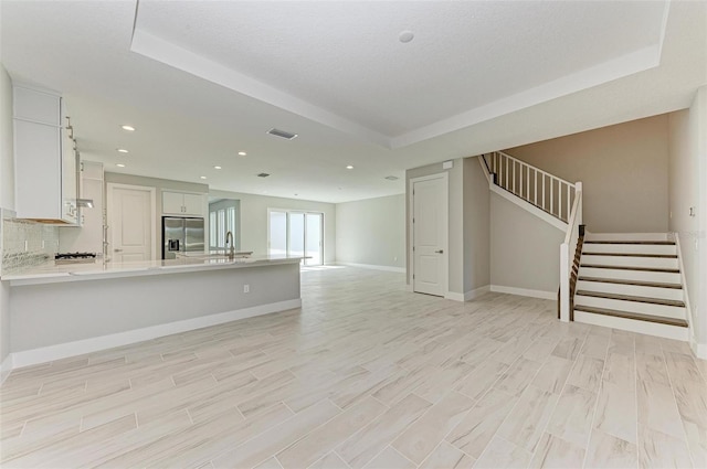 unfurnished living room featuring light wood-type flooring, a raised ceiling, a textured ceiling, and sink