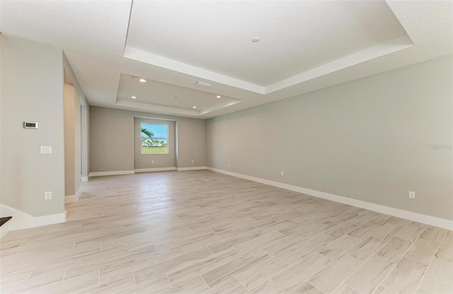 unfurnished room with light wood-type flooring, a tray ceiling, and a textured ceiling