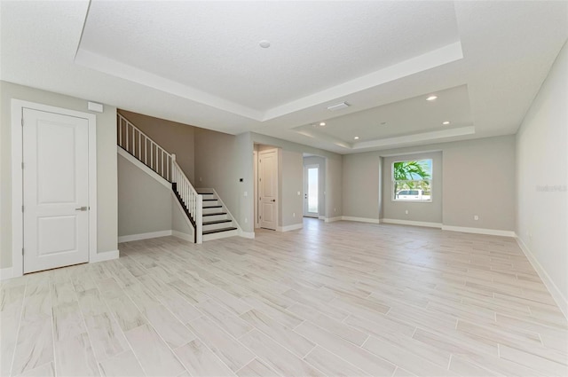 interior space with light wood-type flooring, a raised ceiling, and a textured ceiling