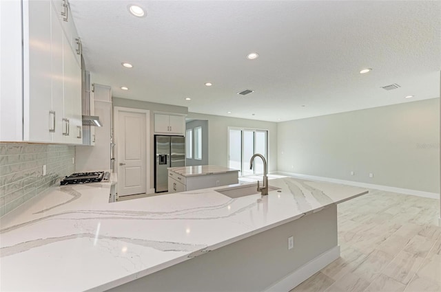 kitchen featuring light stone counters, a center island with sink, stainless steel fridge with ice dispenser, and sink