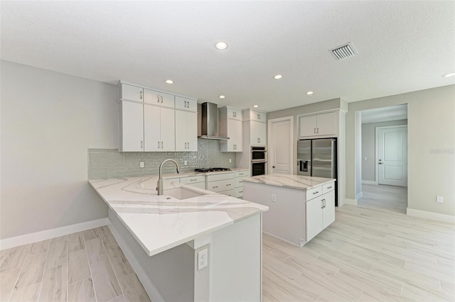 kitchen with a center island, sink, white cabinetry, wall chimney range hood, and appliances with stainless steel finishes