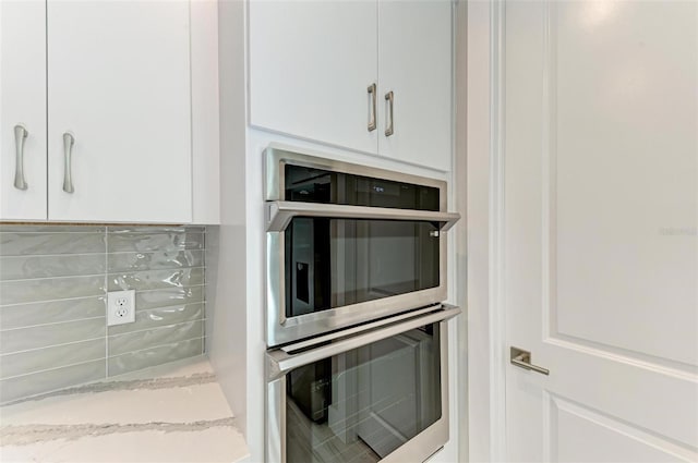 kitchen with light stone countertops, white cabinets, double oven, and tasteful backsplash