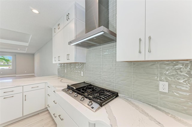 kitchen featuring stainless steel gas stovetop, white cabinets, wall chimney range hood, and decorative backsplash