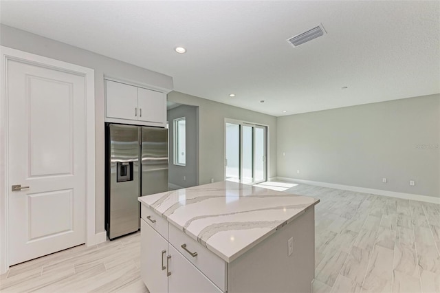 kitchen featuring light stone countertops, white cabinetry, a kitchen island, and stainless steel fridge