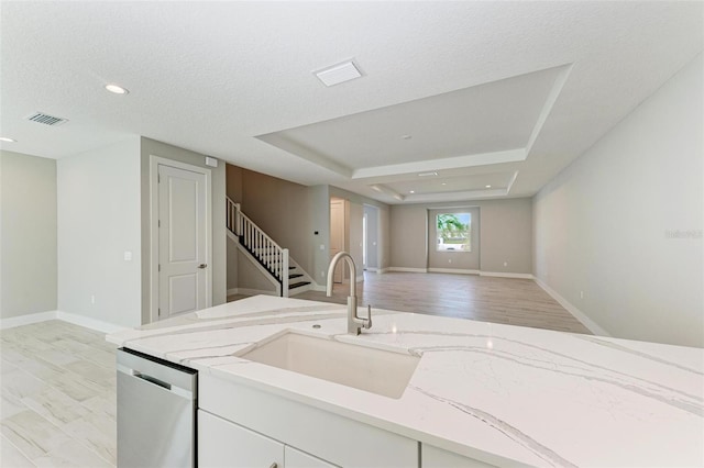 kitchen featuring light stone counters, white cabinets, stainless steel dishwasher, a textured ceiling, and light hardwood / wood-style flooring