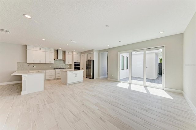 kitchen featuring light hardwood / wood-style flooring, wall chimney range hood, white cabinetry, appliances with stainless steel finishes, and a center island