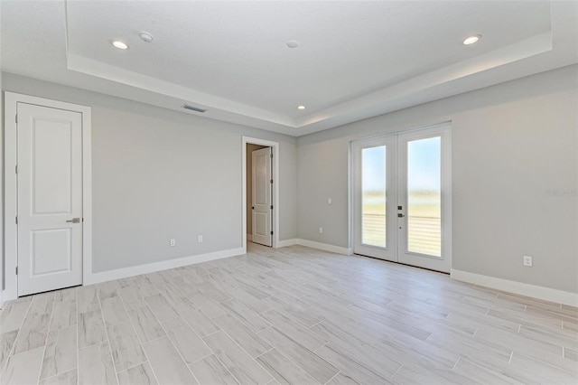 spare room with light hardwood / wood-style flooring, a raised ceiling, and french doors