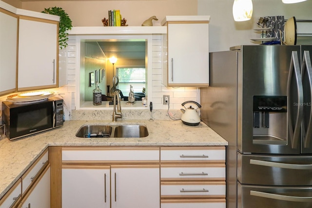 kitchen with stainless steel refrigerator with ice dispenser, white cabinetry, sink, and light stone countertops