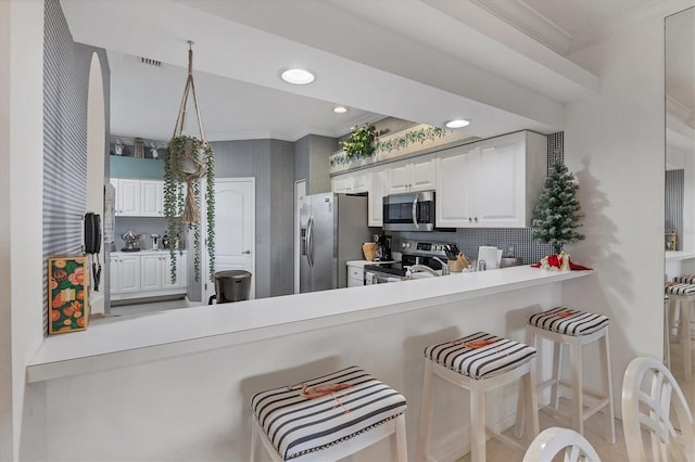 kitchen with white cabinetry, kitchen peninsula, appliances with stainless steel finishes, a kitchen breakfast bar, and tasteful backsplash