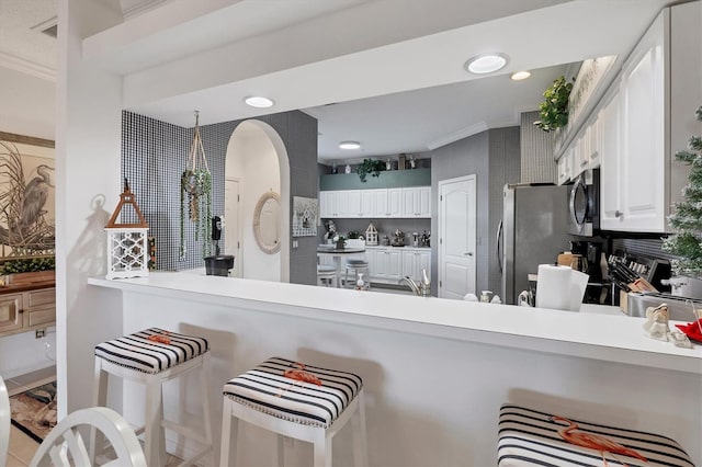 kitchen with kitchen peninsula, appliances with stainless steel finishes, ornamental molding, and white cabinets