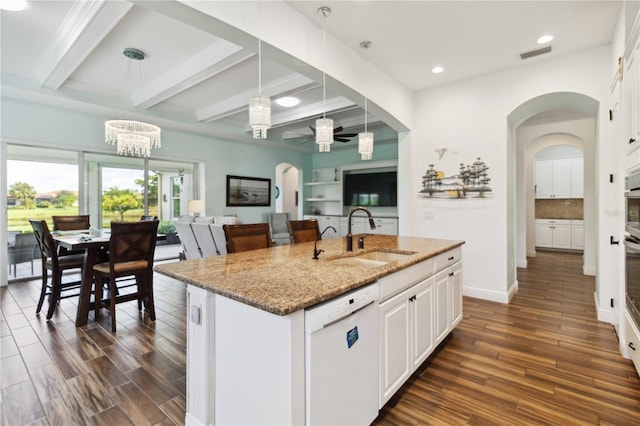 kitchen with light stone counters, an island with sink, white dishwasher, decorative light fixtures, and sink