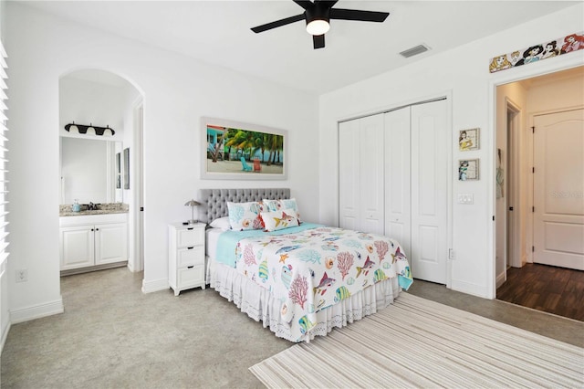 bedroom with a closet, ceiling fan, light colored carpet, and connected bathroom