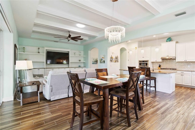 dining space with ceiling fan with notable chandelier, beam ceiling, ornamental molding, and hardwood / wood-style flooring