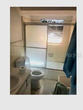 full bathroom featuring tile walls, shower / bath combination with glass door, toilet, and vanity