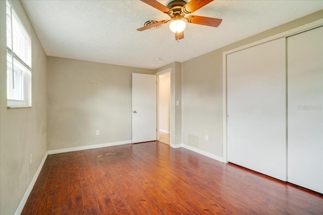 unfurnished bedroom with ceiling fan, a textured ceiling, a closet, and dark wood-type flooring