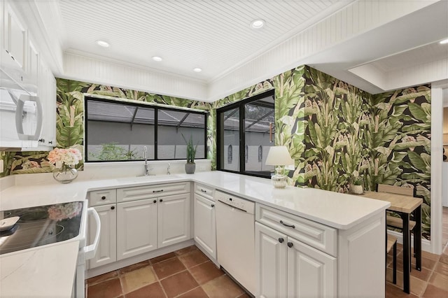 kitchen featuring light countertops, white cabinets, a sink, white appliances, and a peninsula