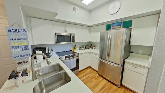 kitchen with white cabinets, sink, appliances with stainless steel finishes, and light hardwood / wood-style flooring