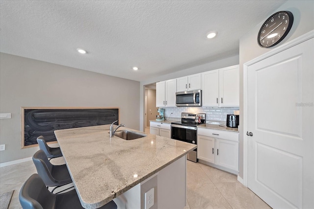 kitchen with white cabinets, sink, a center island with sink, appliances with stainless steel finishes, and a kitchen bar