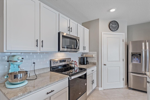 kitchen with light stone counters, white cabinets, light tile patterned floors, backsplash, and appliances with stainless steel finishes