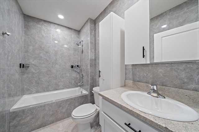 full bathroom with tile walls, tiled shower / bath combo, vanity, and toilet