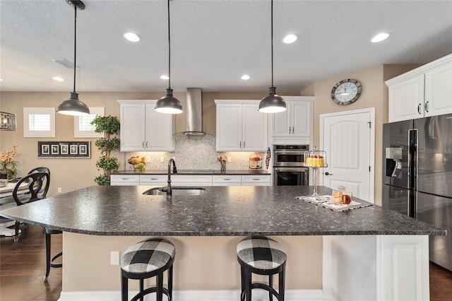 kitchen featuring sink, a center island with sink, wall chimney range hood, and appliances with stainless steel finishes