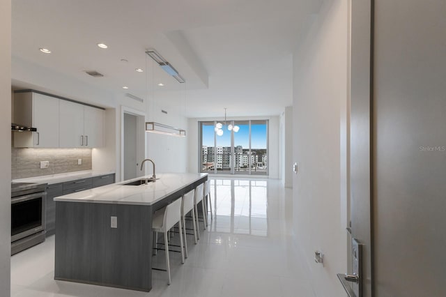 kitchen featuring white cabinetry, an island with sink, tasteful backsplash, decorative light fixtures, and stainless steel electric range oven