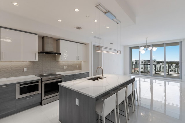 kitchen with white cabinets, hanging light fixtures, sink, a center island with sink, and stainless steel appliances