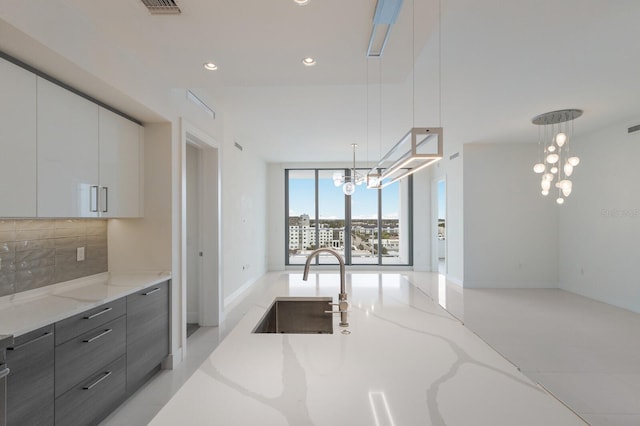 kitchen featuring pendant lighting, white cabinets, light stone counters, and tasteful backsplash