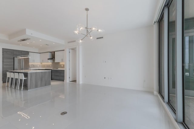 kitchen featuring an island with sink, hanging light fixtures, light tile patterned floors, stainless steel fridge, and a chandelier