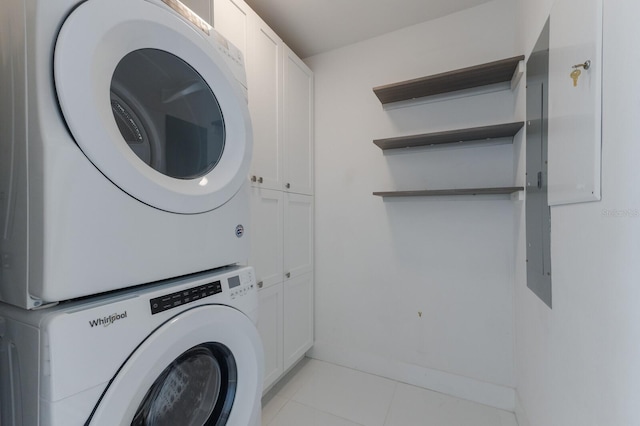 clothes washing area featuring stacked washer and clothes dryer, cabinets, and light tile patterned flooring