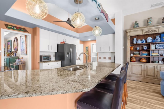 kitchen with stainless steel fridge, sink, white cabinetry, and hanging light fixtures